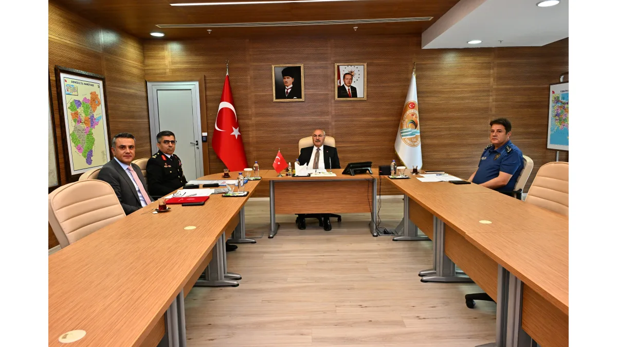 Toplantı masasının etrafında oturan yetkililer ve ortada masa başında bulunan kişi yer alıyor.