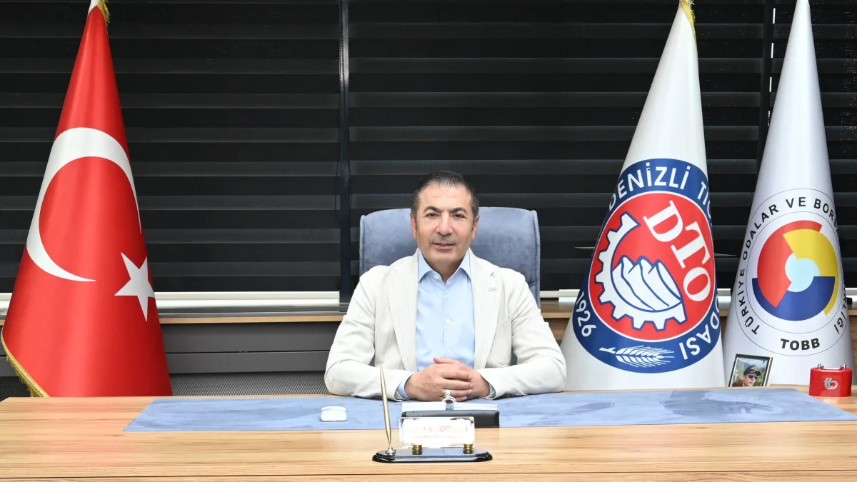Makam masasında oturan erkek ve arkasında Türk bayrağı ile Denizli Ticaret Odası bayrakları