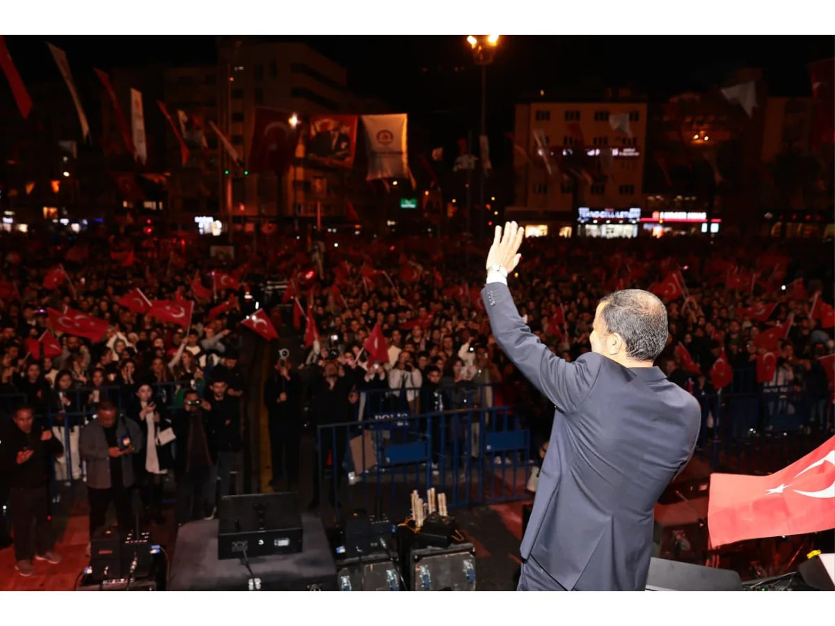 Gecenin karanlığında kalabalığa el sallayan bir kişi ve ellerinde Türk bayrakları olan yürüyüşçüler