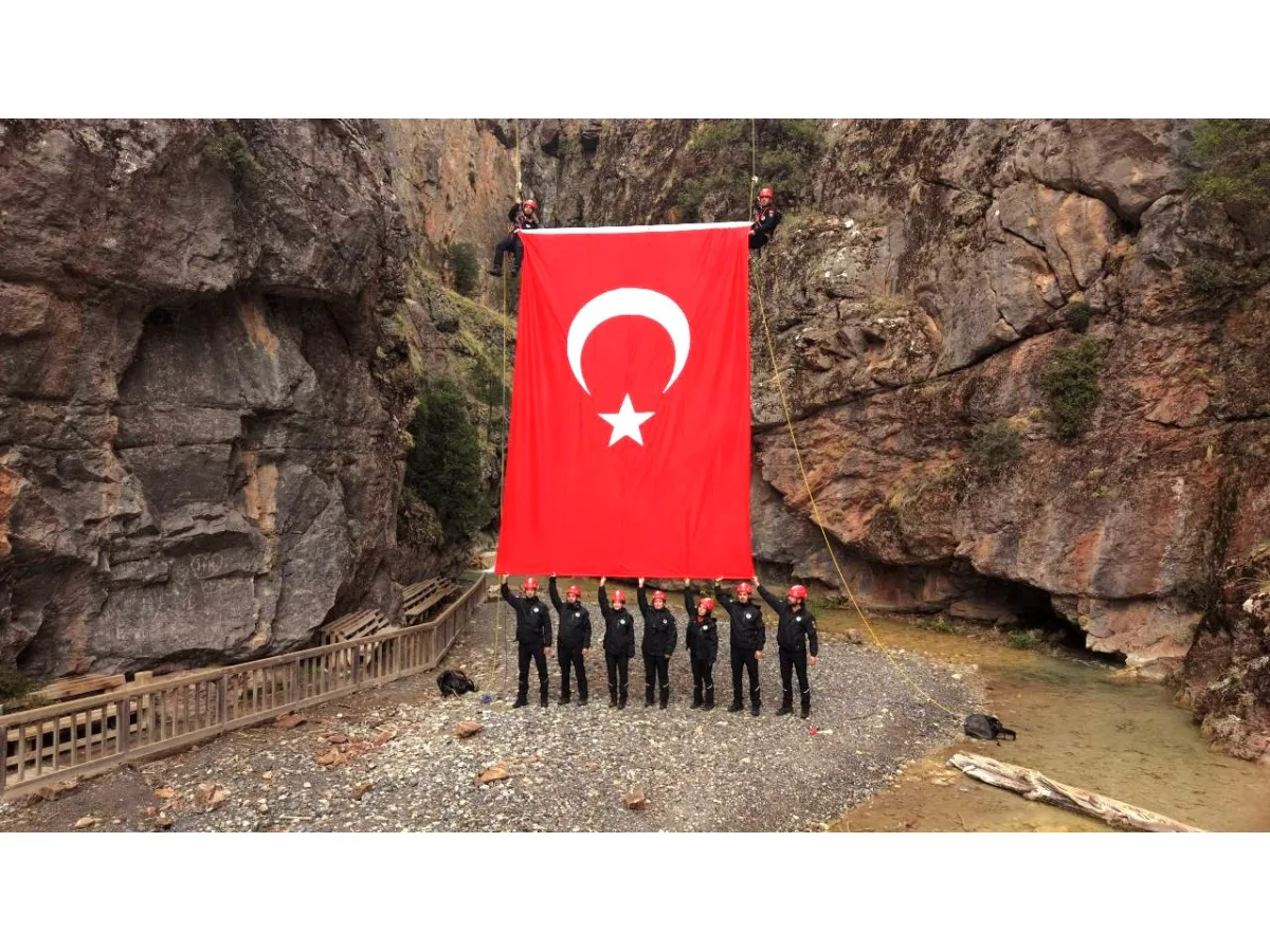 Kayalık bir vadide dev Türk bayrağı tutan görevliler
