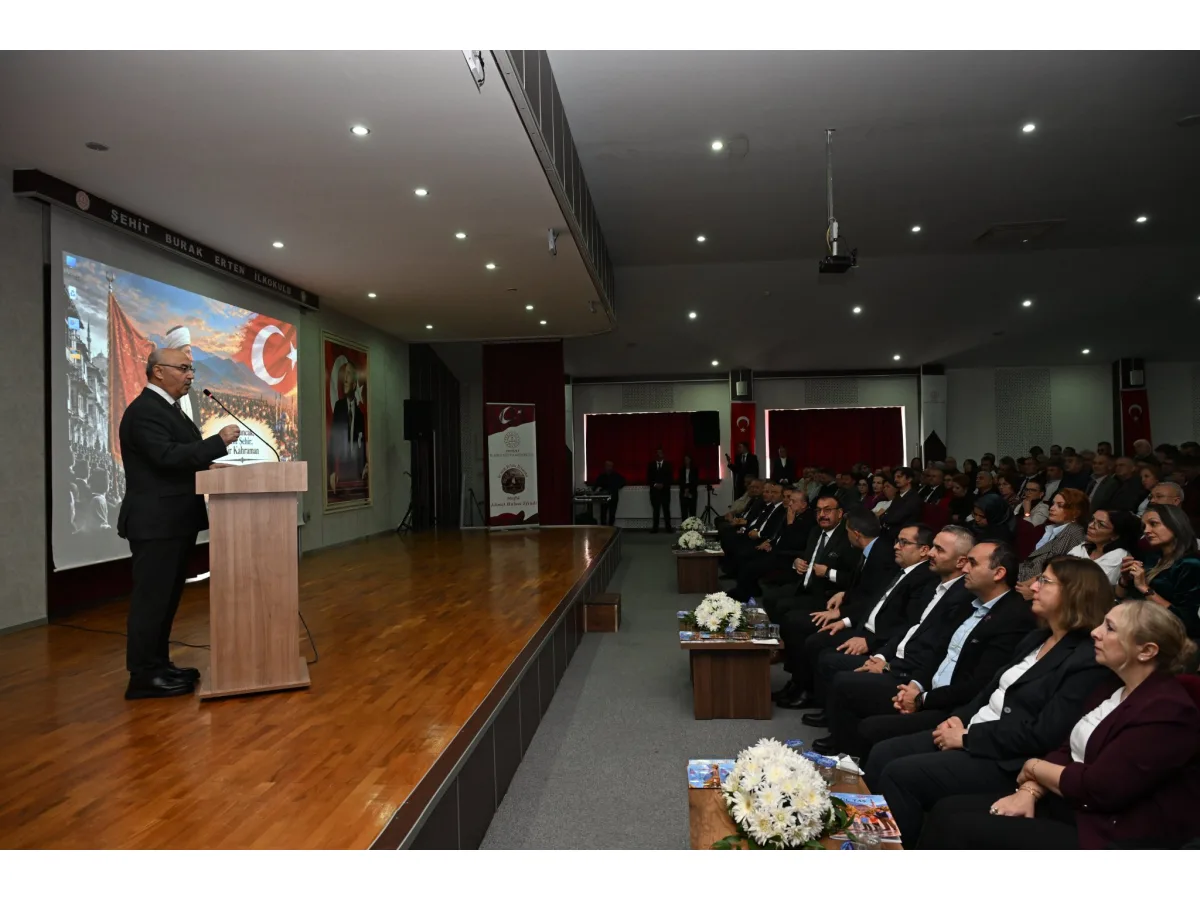 Salondaki kürsüde konuşma yapan bir kişi ve onu izleyen kalabalık