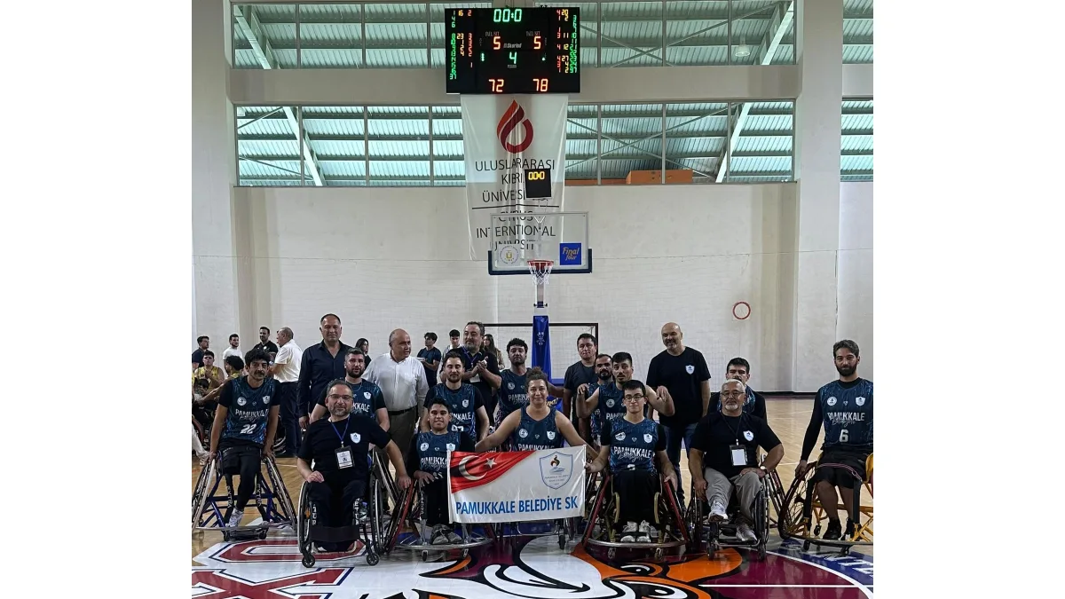 Pamukkale Belediyesi SK tekerlekli sandalye basketbol takımı sporcuları ve teknik heyet salonda Türk bayrağıyla poz veriyor.
