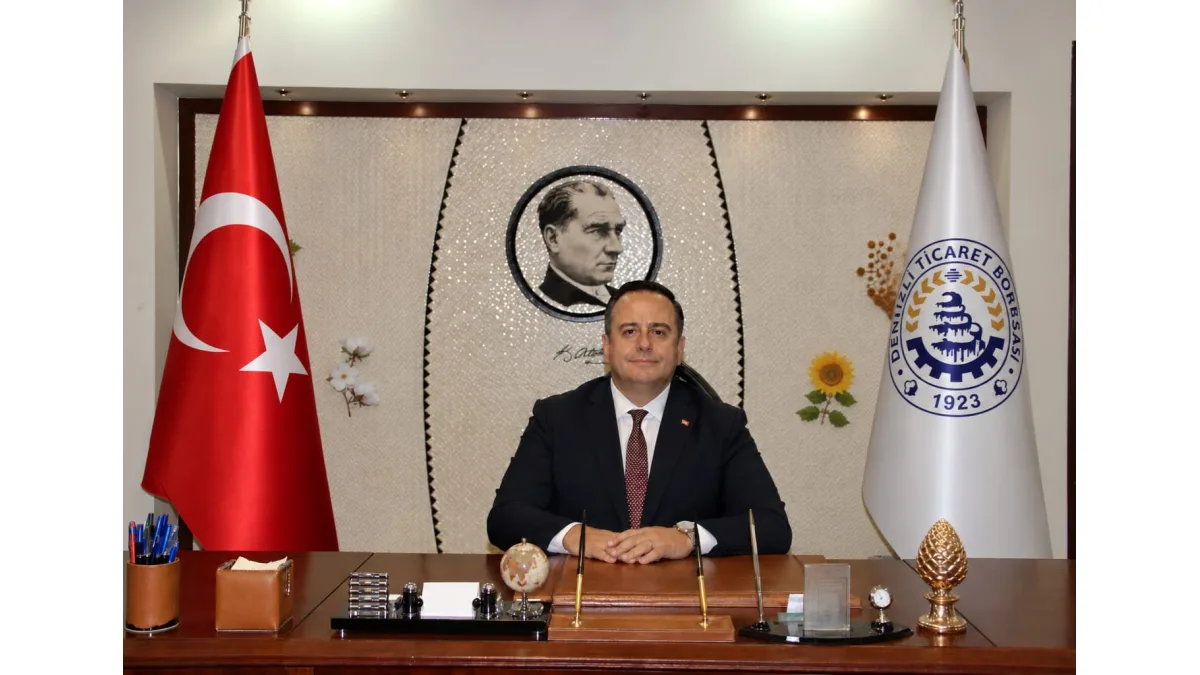 Makresinde oturan bir yetkili, arkasında Türk bayrağı, Denizli Ticaret Borsası bayrağı ve Atatürk portresiyle görülüyor.