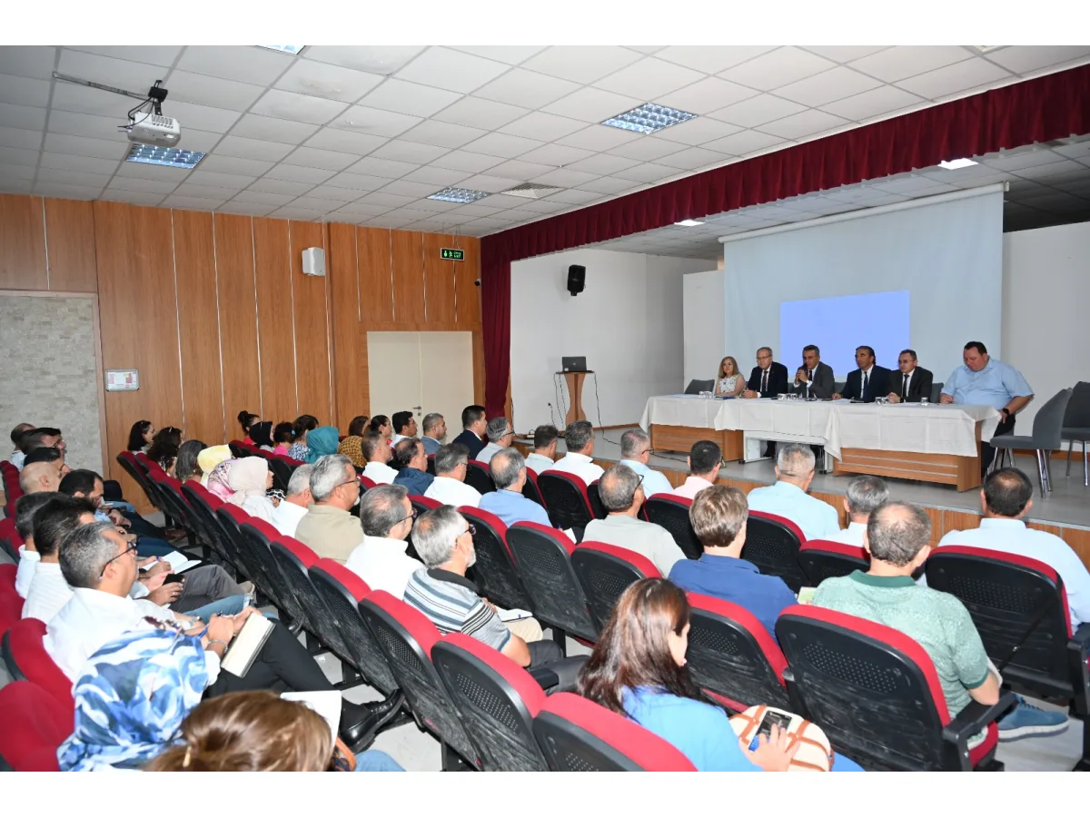 Konferans salonunda koltuklarda oturan katılımcılar ve sahilde masada duran yetkililer görülüyor